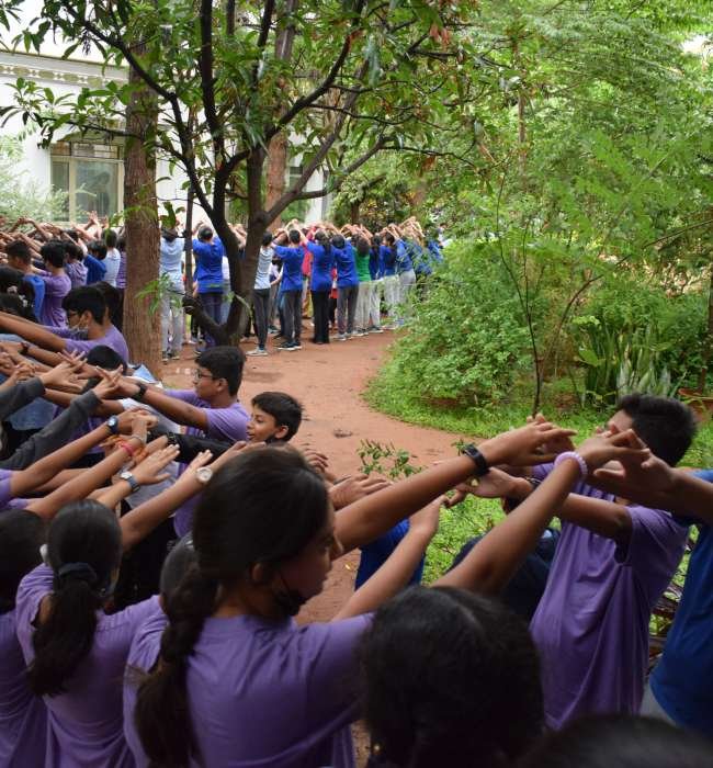 Students of Sloka assembled outside in two rows facing each other with hands raised across to each other.