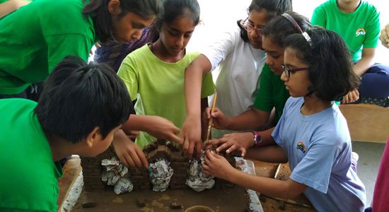A group of Sloka students work with clay blocks standing around a desk.