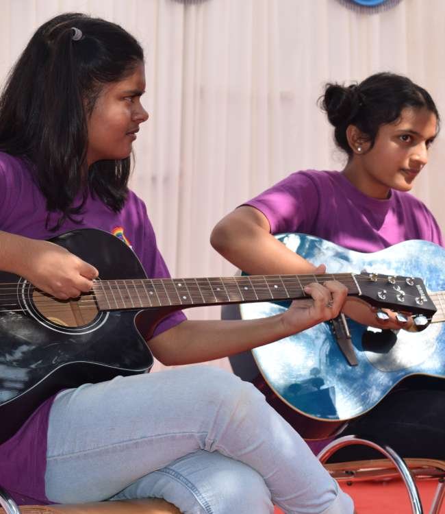 Two high school students sit on chairs holding guitars.