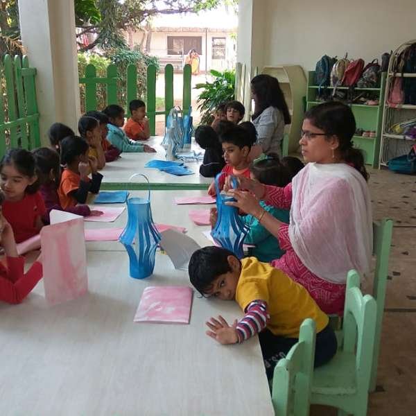 Students seated around tables in an open area crafting paper lanterns under the guidance of a teacher.