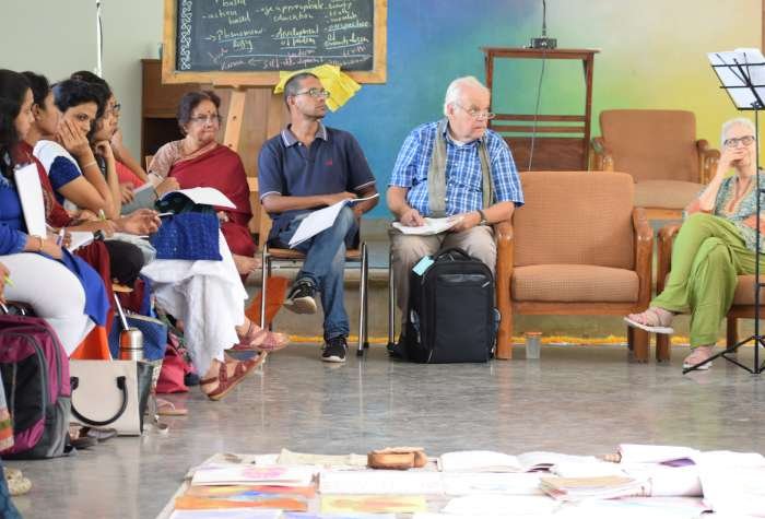 A group of teachers sit in a circle indoors while one teacher stands addressing them, at an International Teachers’ workshop by Christof Wiechert.